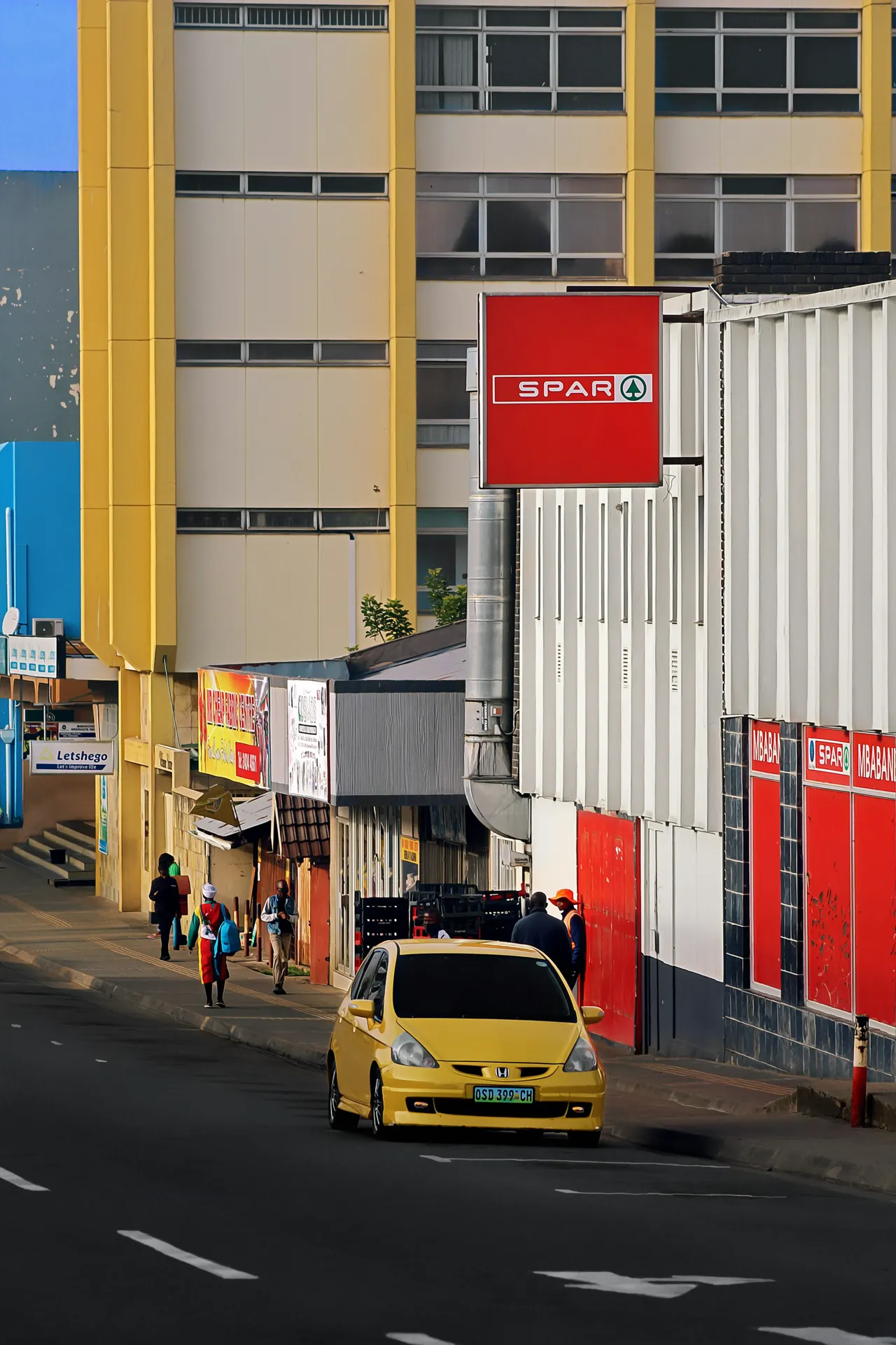 A yellow car drives down a street near a spar store