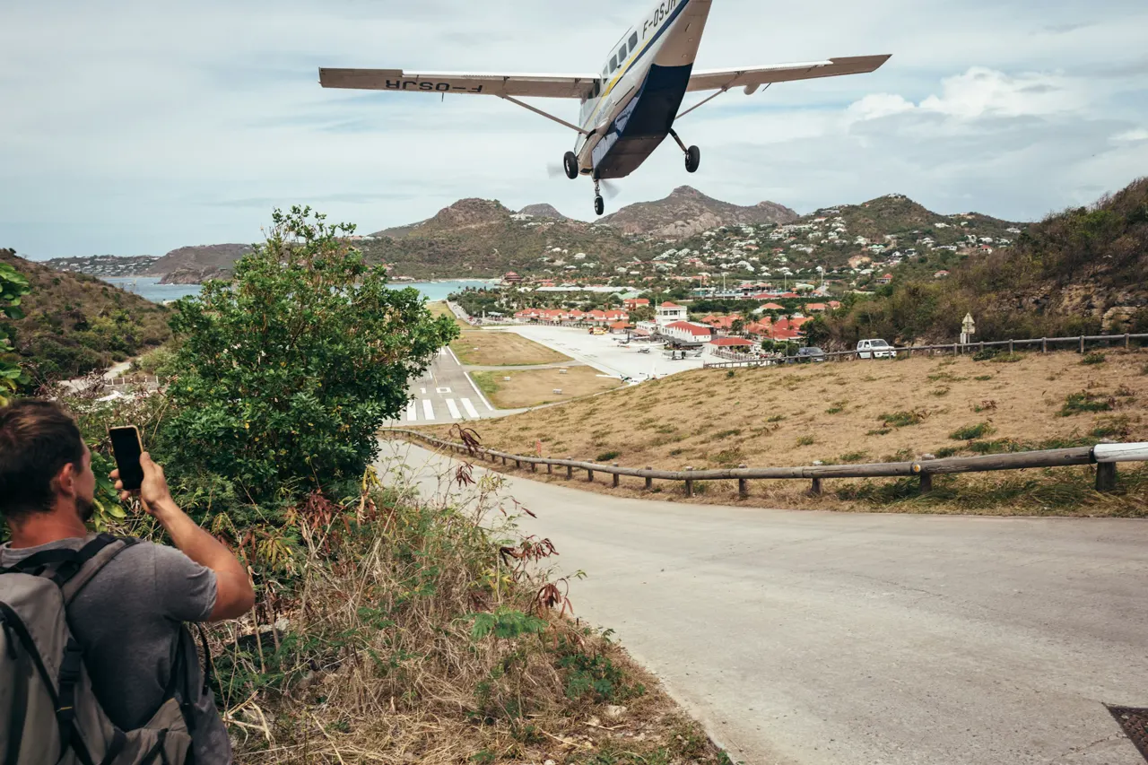 Man photographs small airplane landing on runway