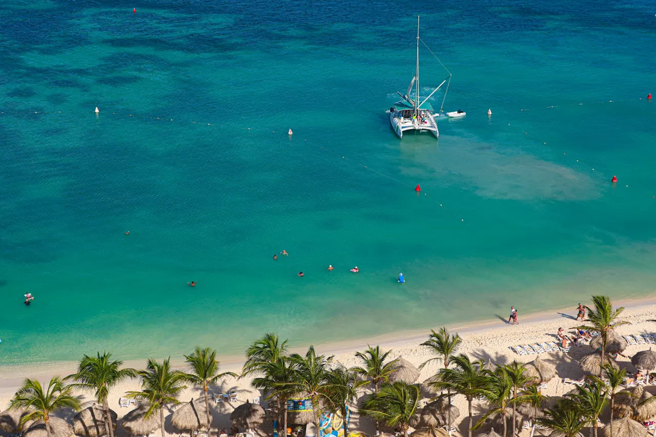 Catamaran sailing in clear turquoise ocean water near beach