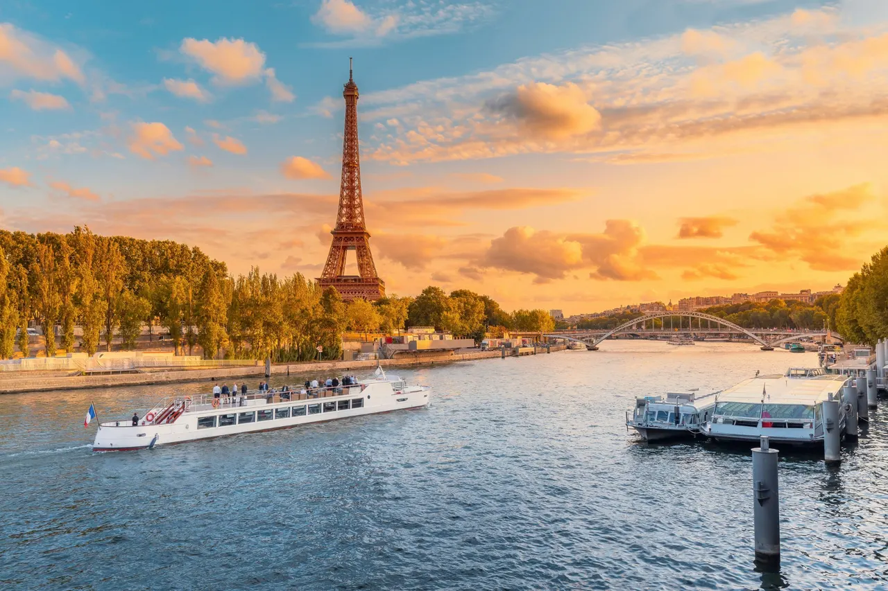 The main attraction of Paris and all of Europe is the Eiffel tower in the rays of the setting sun on the bank of Seine river with cruise tourist ships