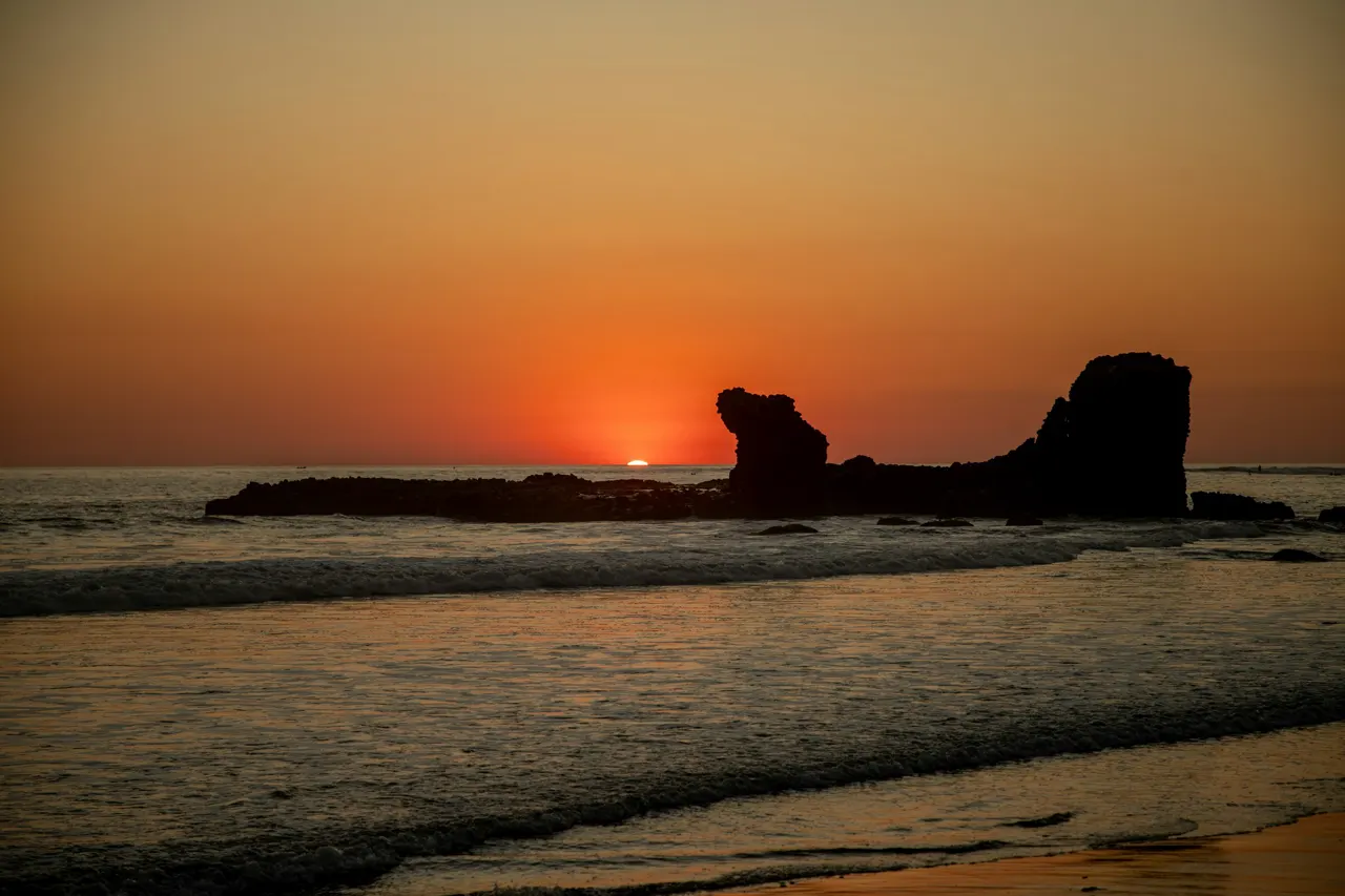 silhouette of rock formation on sea during sunset