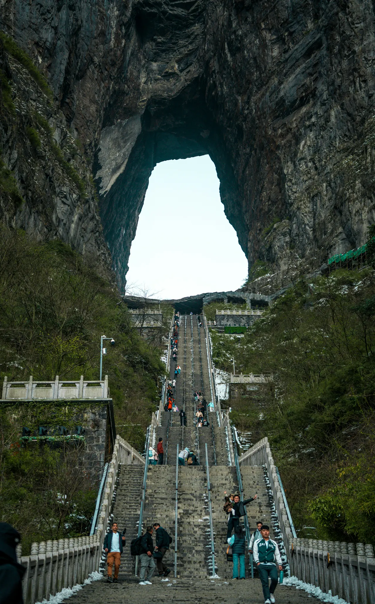 People climb a long staircase towards a rock arch