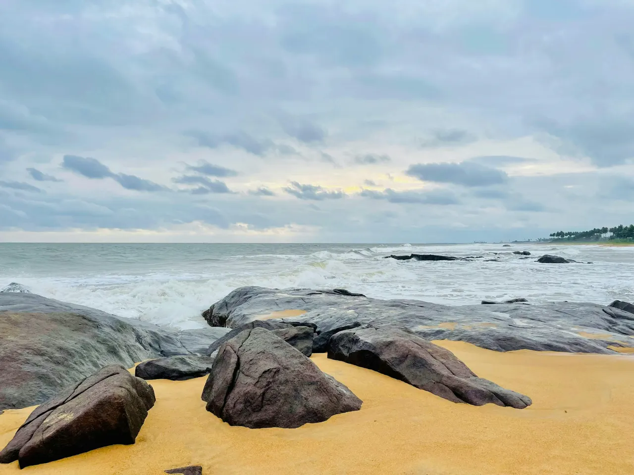 A rugged coastal landscape with large, weathered rocks scattered along the sandy shore