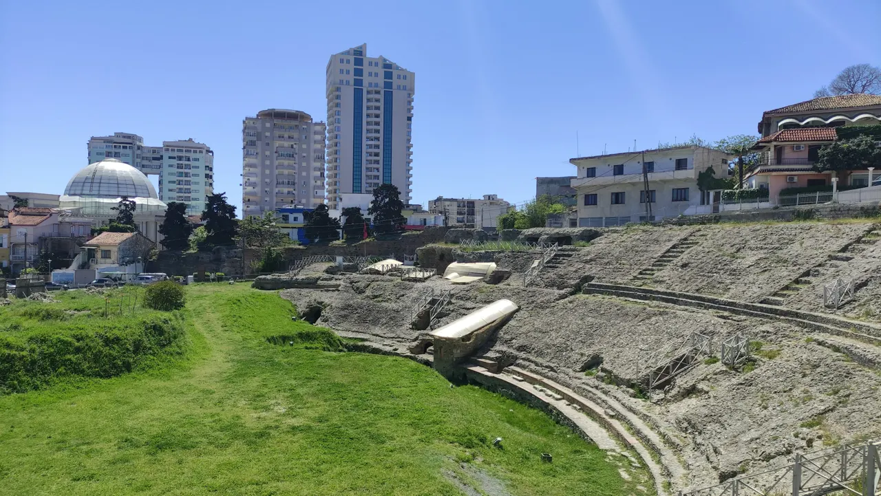 a large stone structure with a dome and a grassy area with buildings in the background