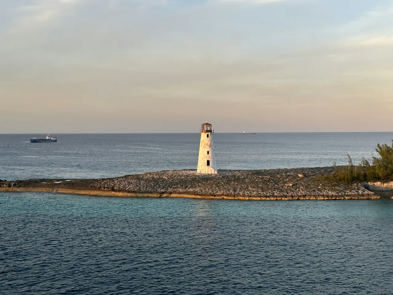 The white Paradise Island Lighthouse stands at the rocky tip of the harbor entrance under a soft evening sky, Nassau, The Bahamas
