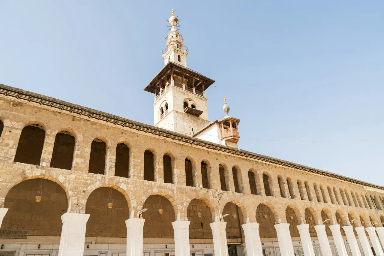 The Umayyad Mosque minaret rising above stone arched colonnades in Damascus, Syria