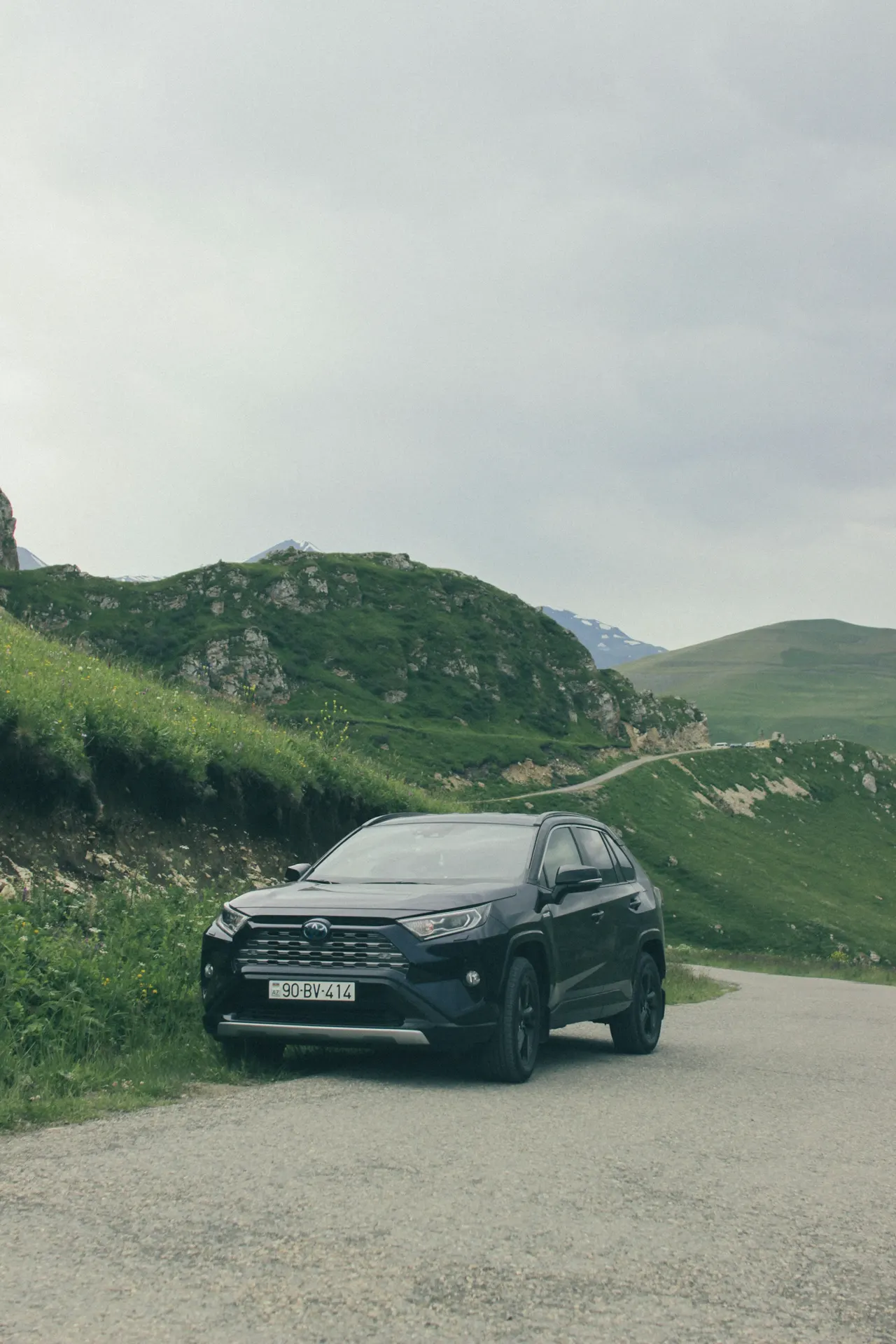 A black car driving down a road next to a lush green hillside