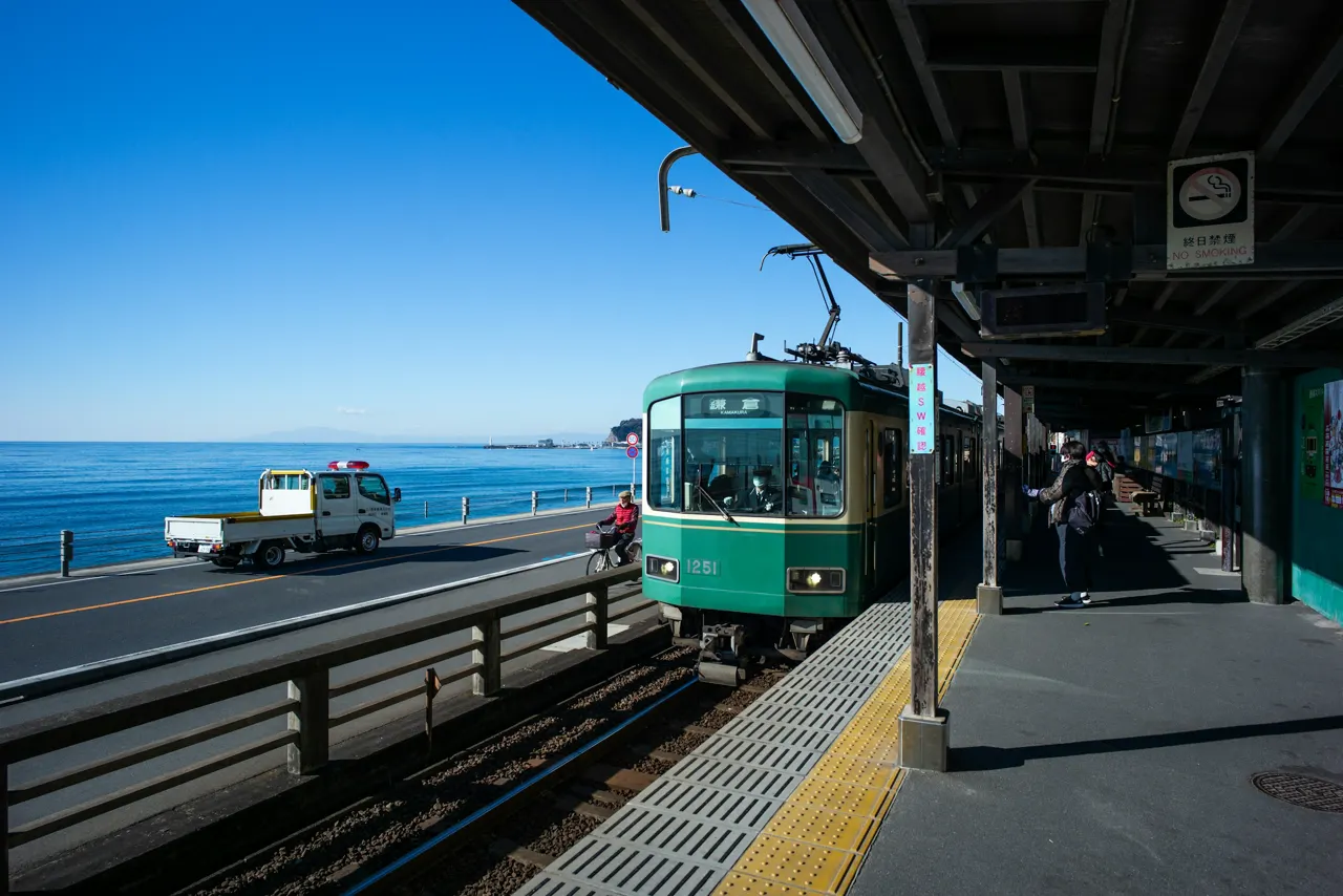 a green train traveling down tracks next to the ocean