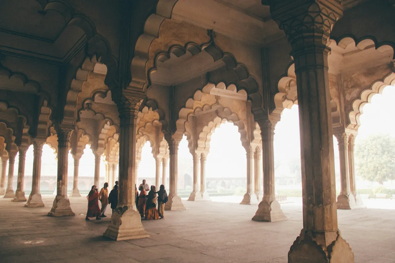 People walking through a stone pavilion with arched columns at the Red Fort