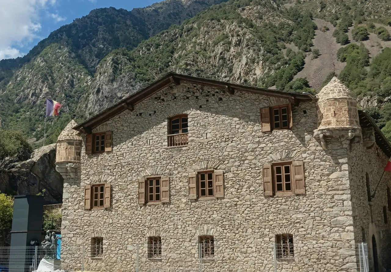 A stone building with wooden shutters against a steep mountain slope