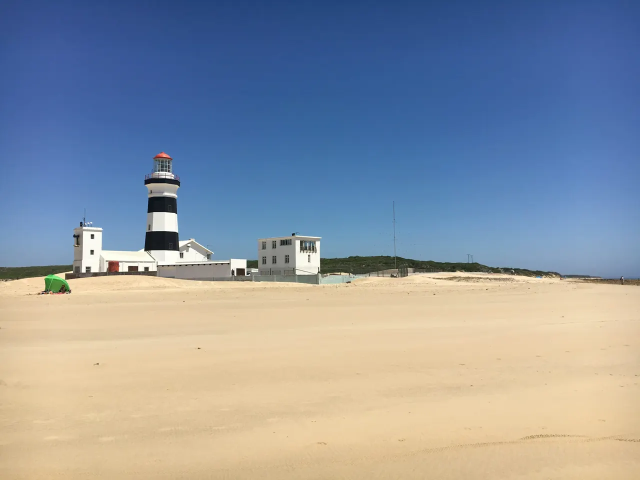 white and black concrete lighthouse on brown sand under blue sky during daytime