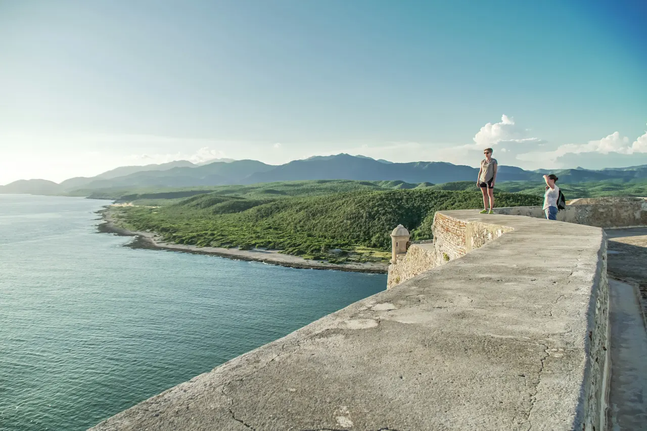 man in white t-shirt and brown shorts standing on concrete dock near body of water