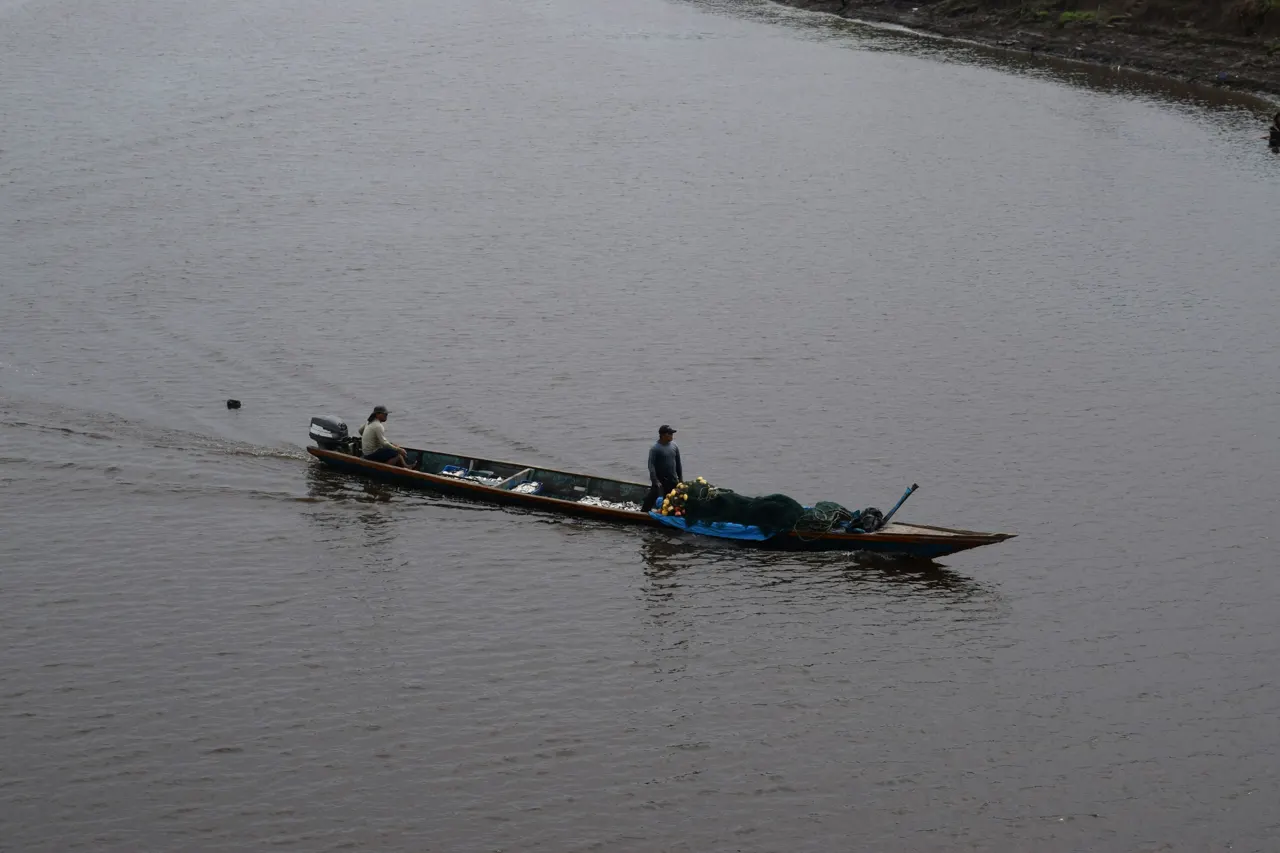 Two people in a long narrow boat with fishing nets on a river